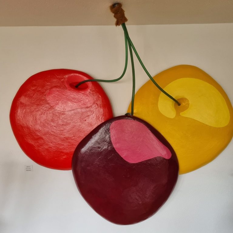 Trois fruits colorés en forme de cerises accrochés au mur.