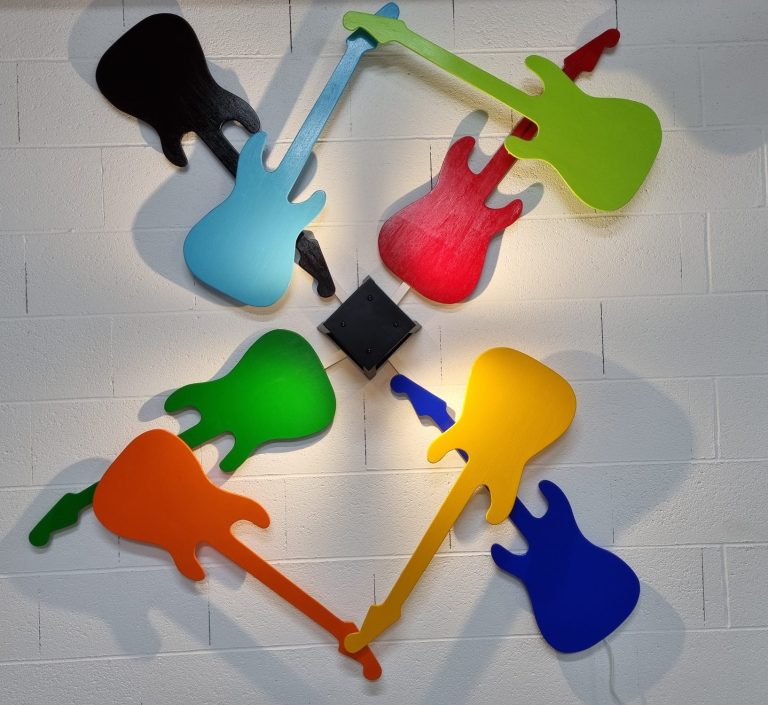 Guitares colorées disposées de manière artistique sur un mur blanc.