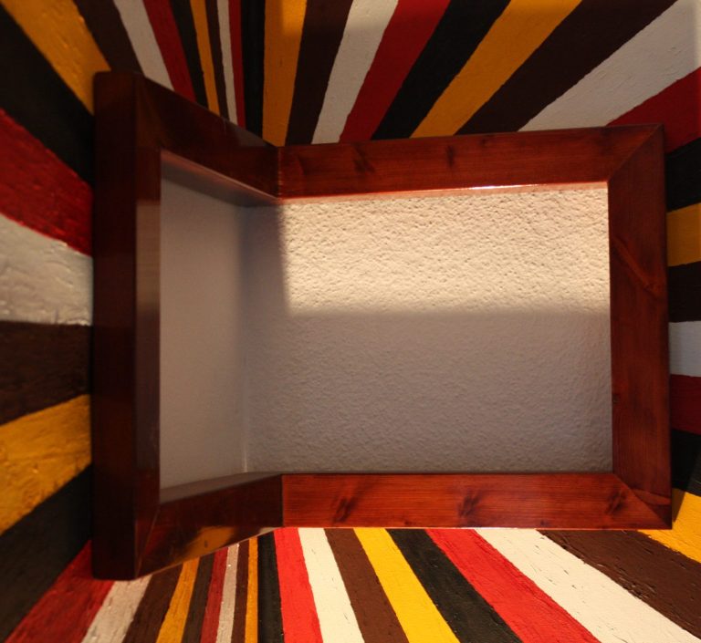 Cadre en bois posé sur un mur rayé de couleurs vives.