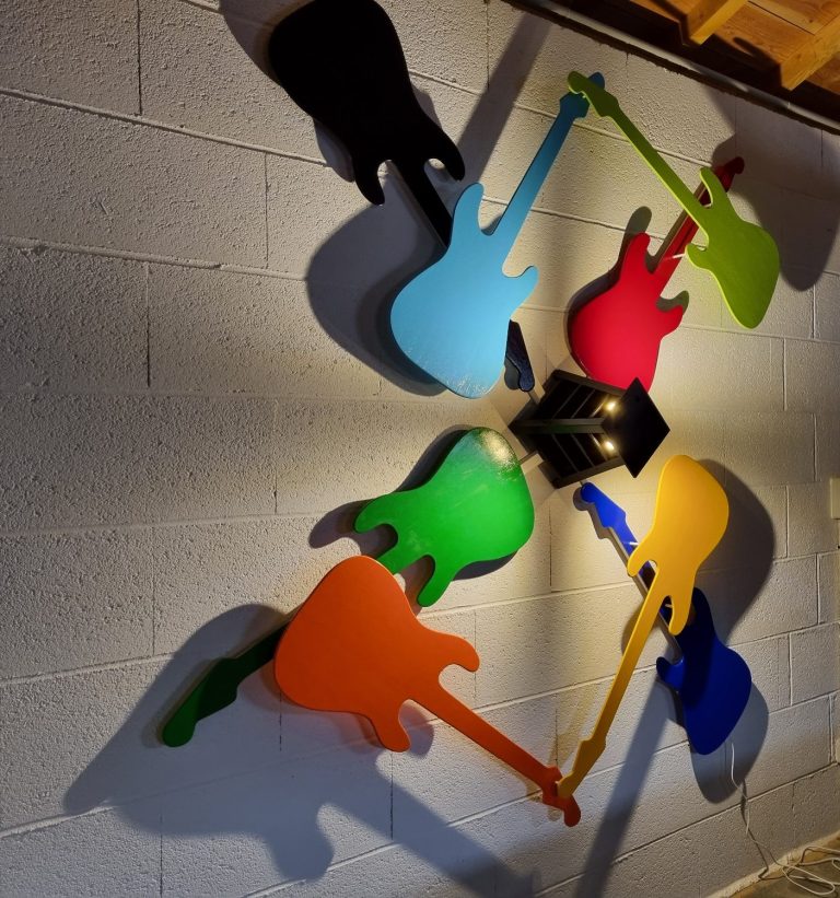 Silhouettes de guitares colorées en ombre sur un mur gris.