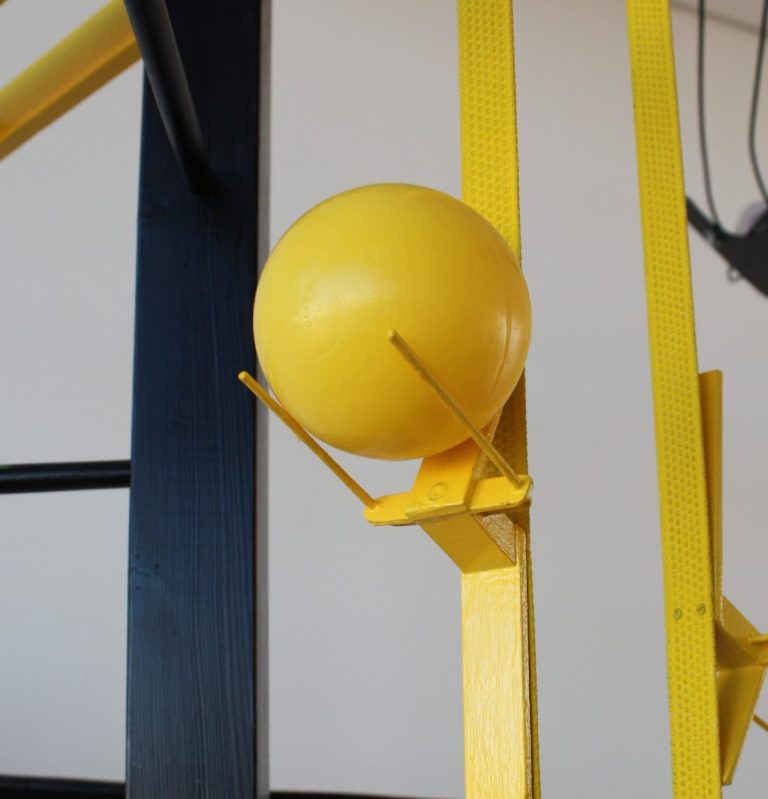 Boule jaune fixée sur une structure en métal, avec des supports jaunes.