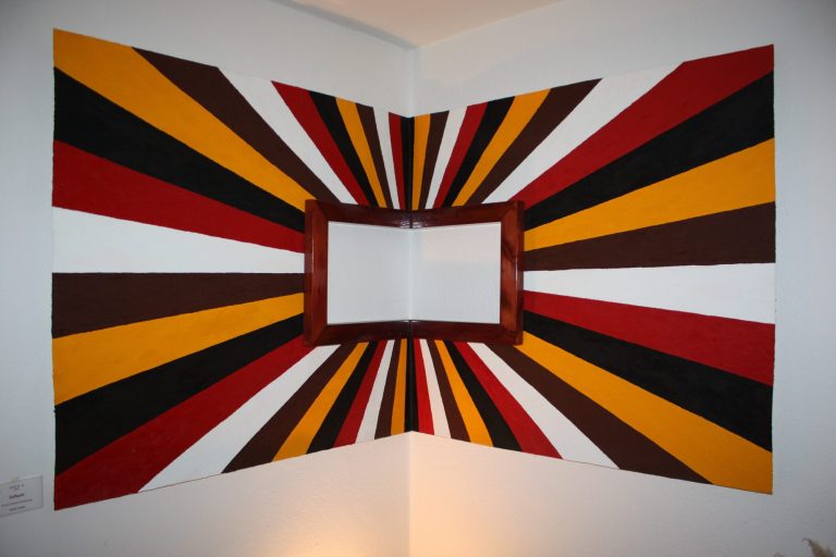 Mur d'angle décoré de bandes de couleurs vives, avec un cadre vide au centre.