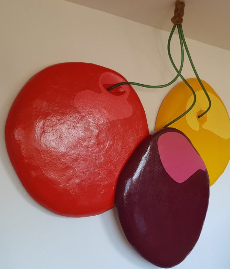 Trois formes colorées suspendues : rouge, jaune et violet, avec des cordes vertes.